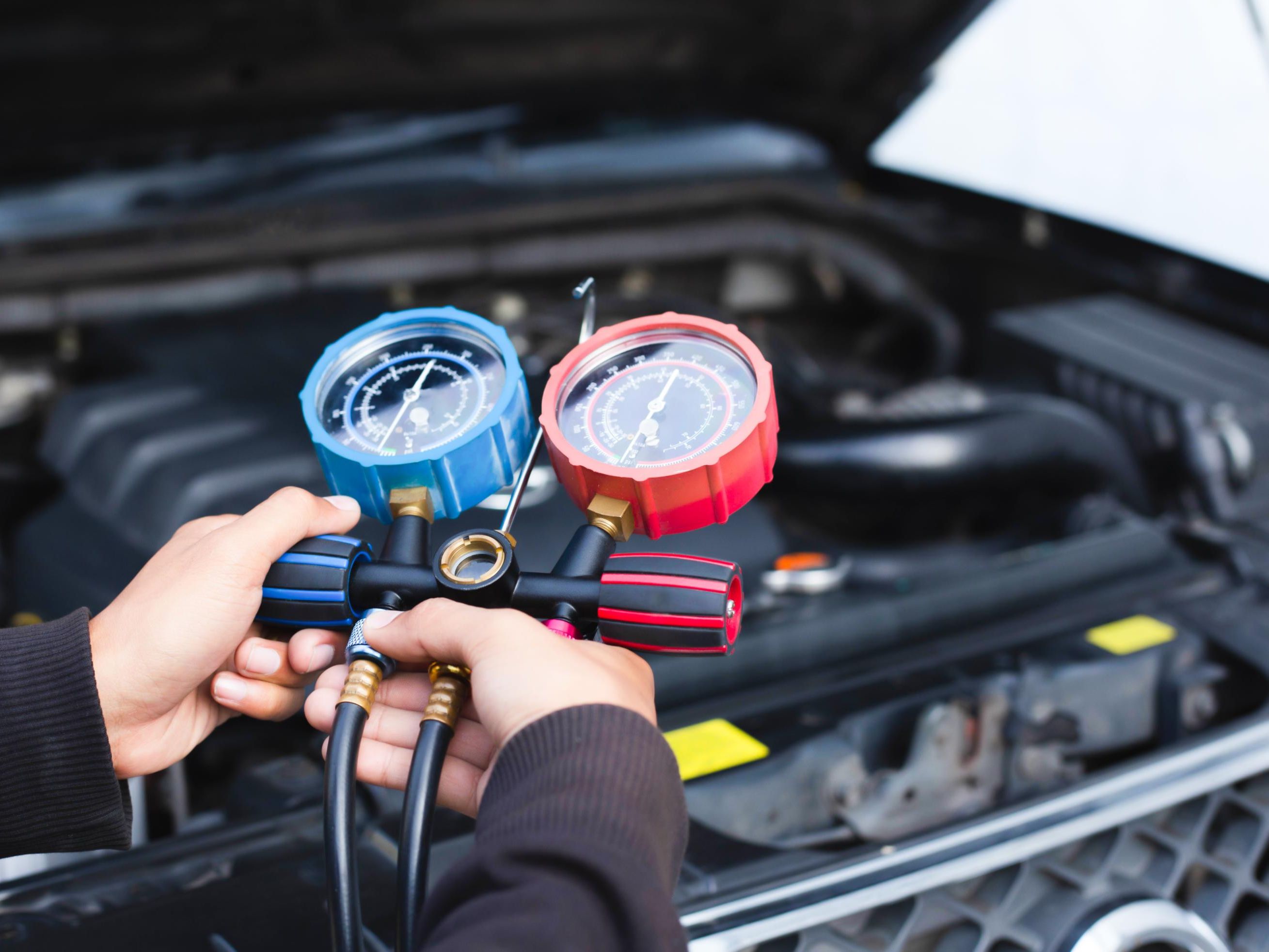 Person bruker et manometer for å måle trykket i bilens klimaanlegg med motorrommet åpent