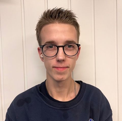 Mann i blå genser foran hvit trevegg